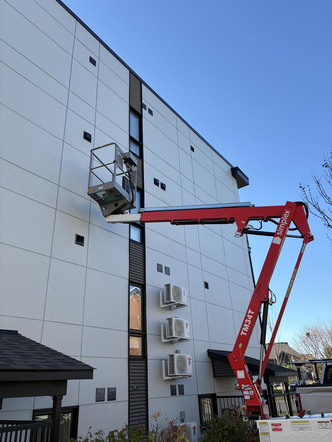 Boom lift raised against a multi-storey building wall lined with worn vent covers before replacement