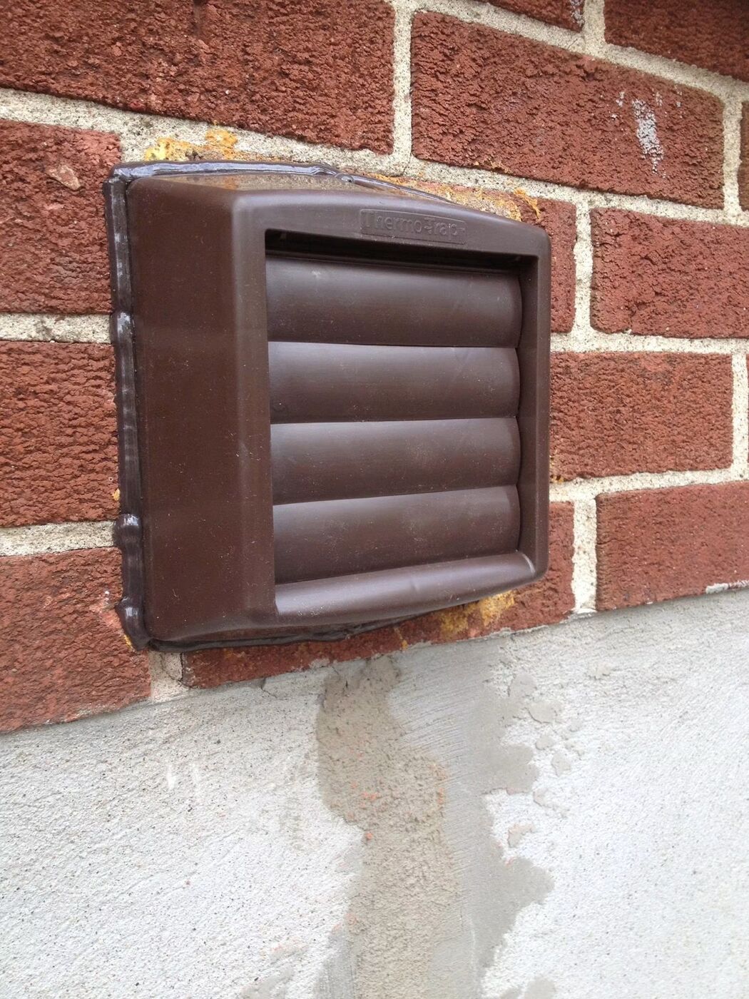 Brown Thermo-Trap vent cover installed and caulked on a red brick wall