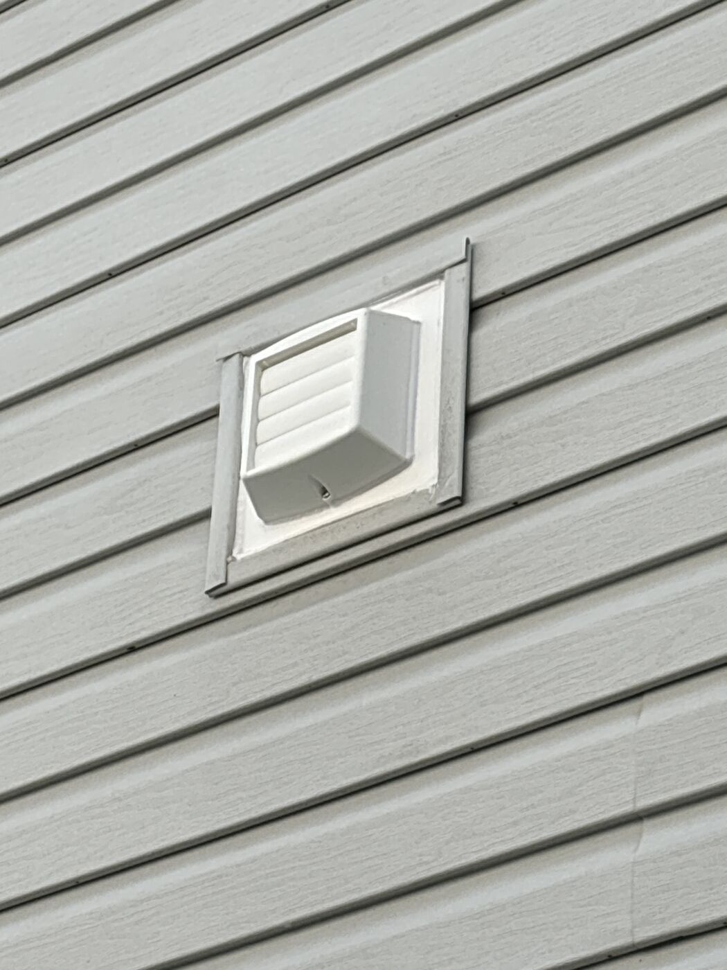 White Thermo-Trap vent set into a colour-matched mounting block on grey lap siding