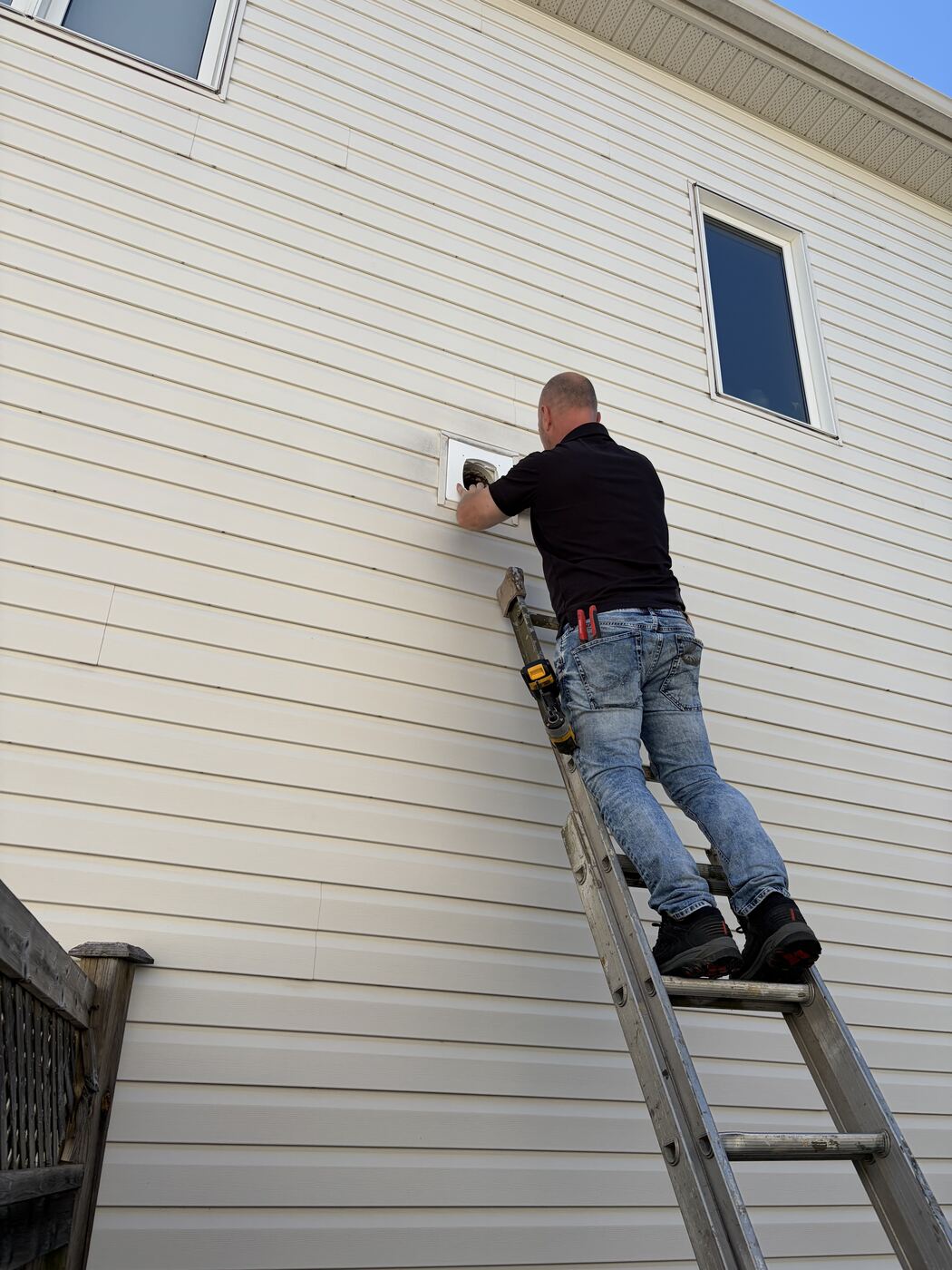 Installer on an extension ladder working on a second-storey wall vent