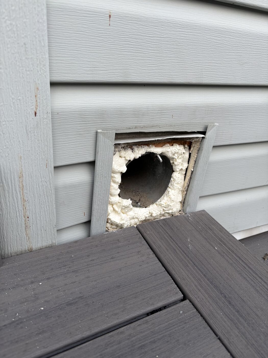 The same wall opening with expanding foam packed around the duct, filling the cavity