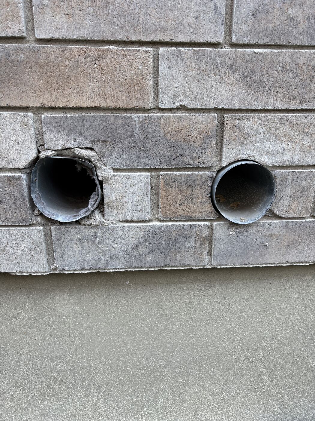 Two bare duct openings in a brick wall before sealing