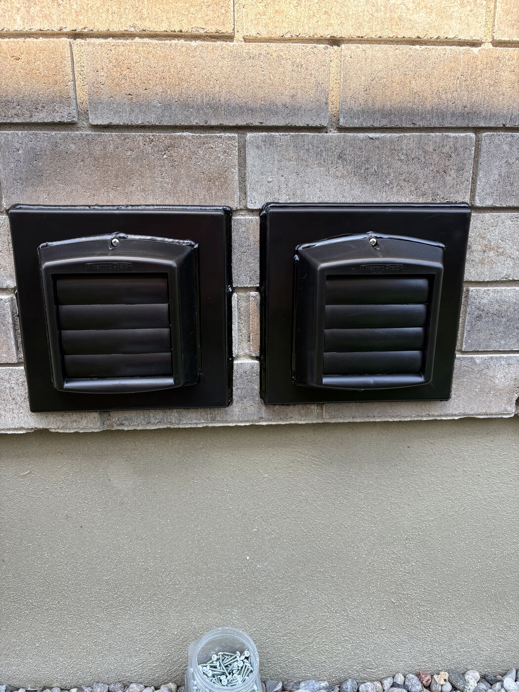 Finished pair of black commercial-grade Thermo-Trap vents on a brick wall