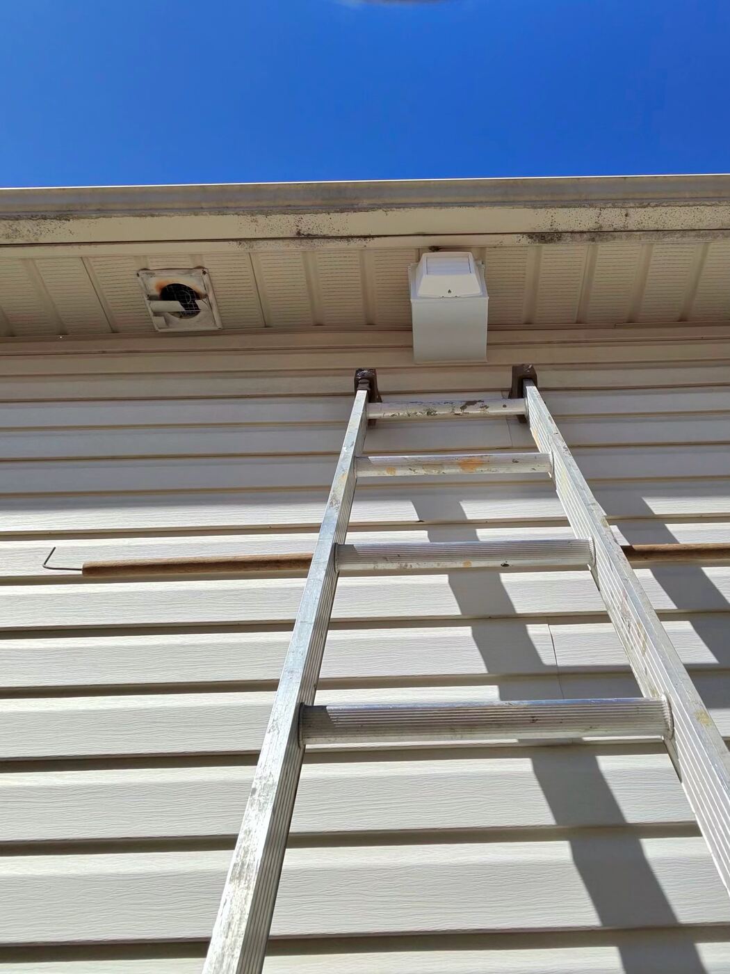 Ladder at the eaves with an old open vent hole beside a newly installed white soffit box