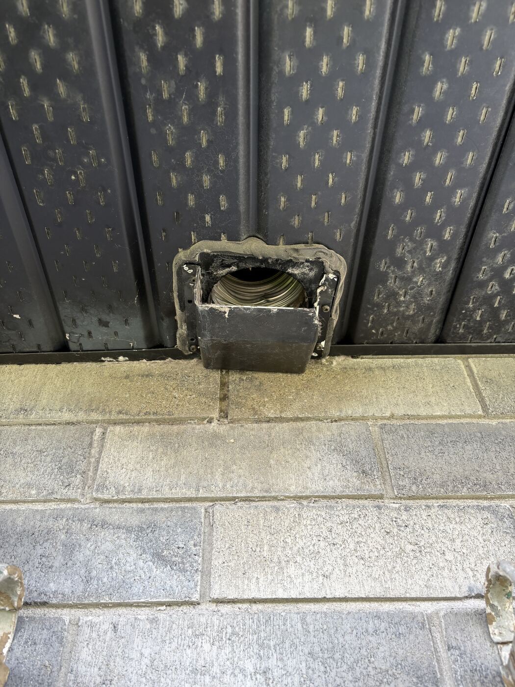 Old grimy soffit vent hood with lint packed in the exposed duct