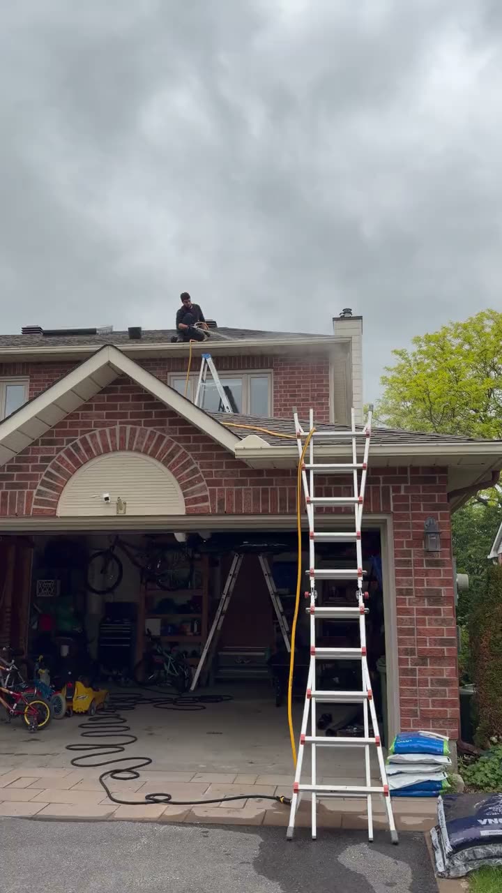 Technician on a ladder cleaning a second-storey gutter on an Ottawa home