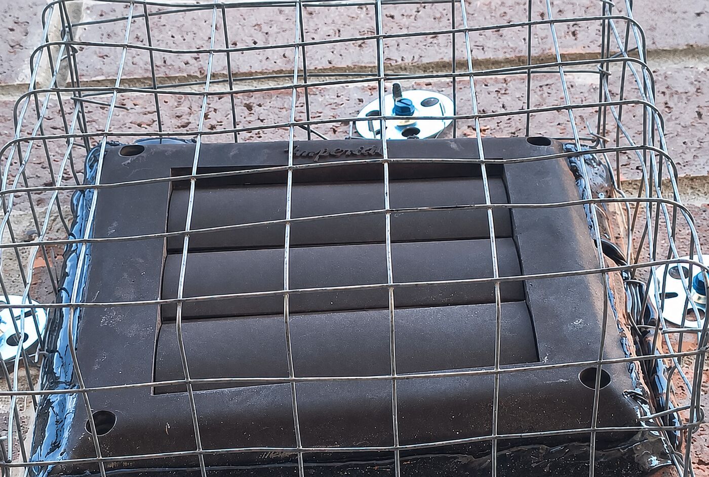 Wire grill cage mounted over an exterior dryer vent cover on a brick wall